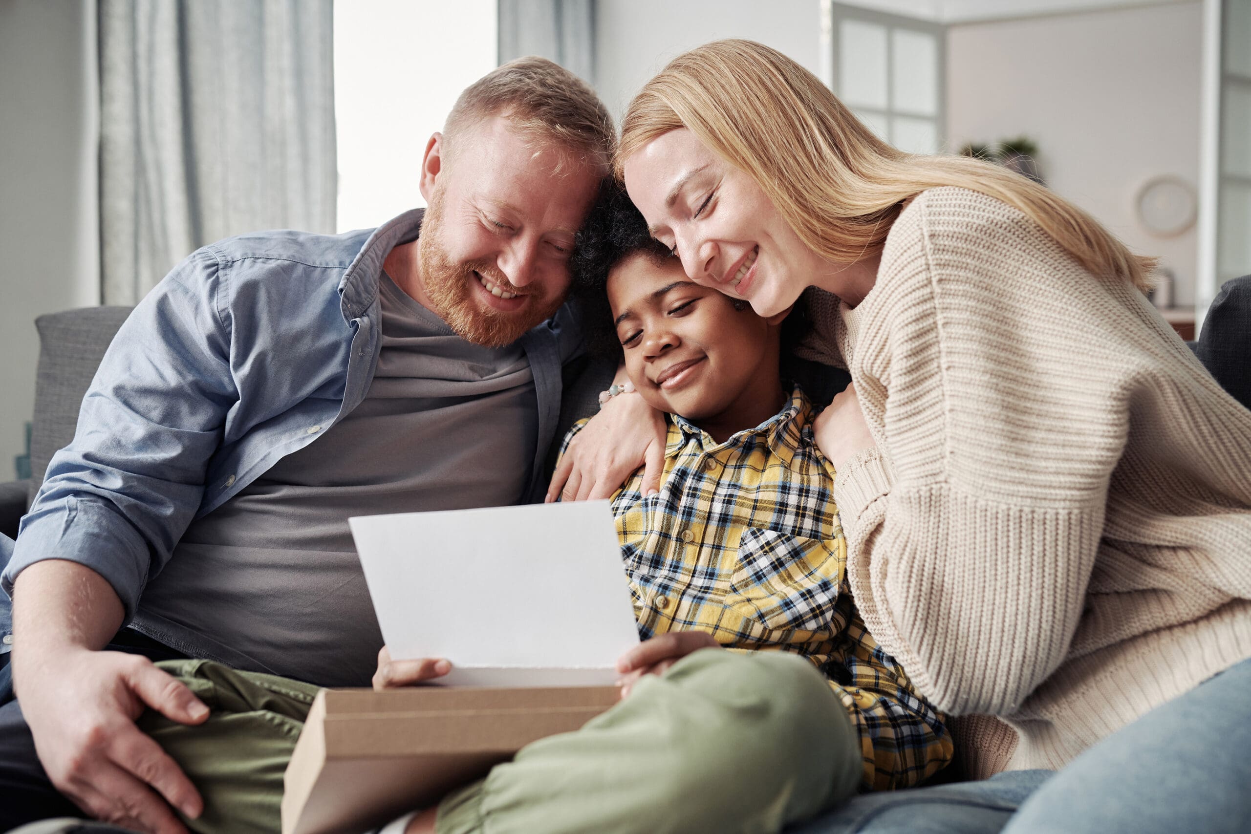 Happy Parents Embracing Their African Adoptive Son While Reading A woman searching on here phone "Will There be Ongoing Contact with the Adoptive Family?"